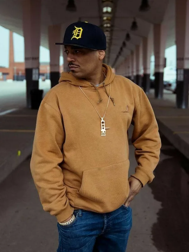 Omar-S wearing a Detroit cap and brown hoodie