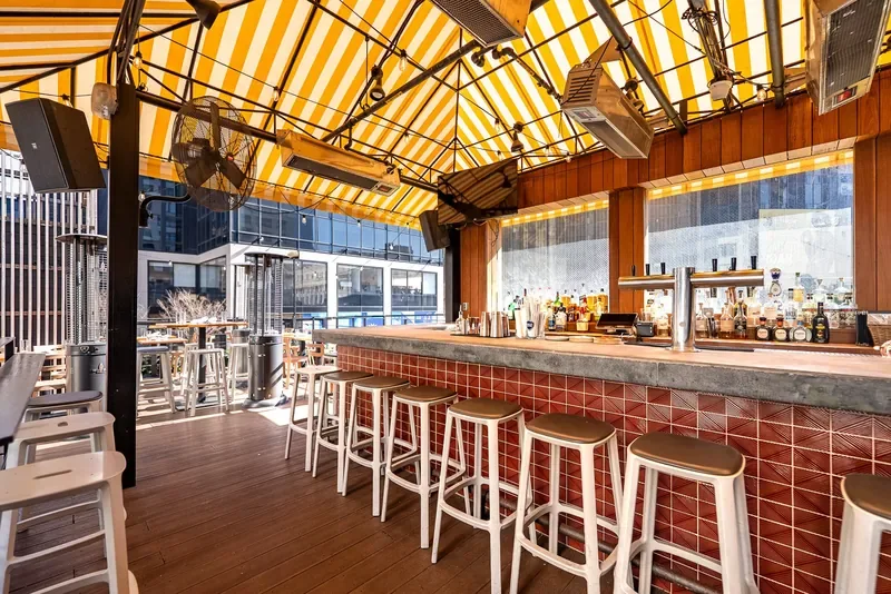 Avenida NYC rooftop bar under yellow-striped awning with Midtown behind