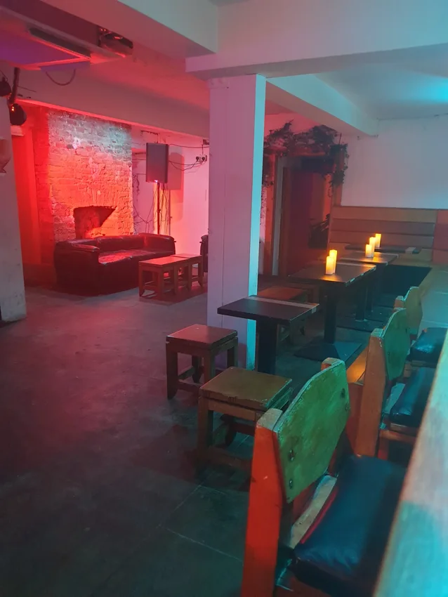 Dalston Den basement lounge with red lighting, brick wall and benches