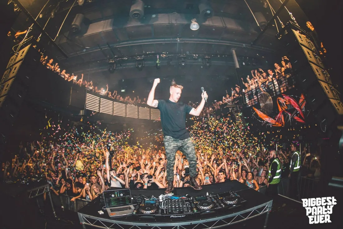 A performer above the DJ booth at Home The Venue, with a packed dancefloor and balcony behind them