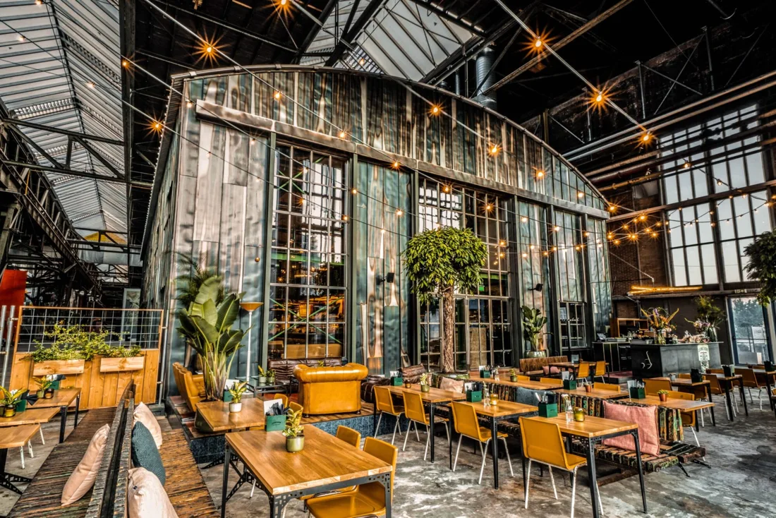 Ijver glass-walled industrial hall interior with tables and string lights