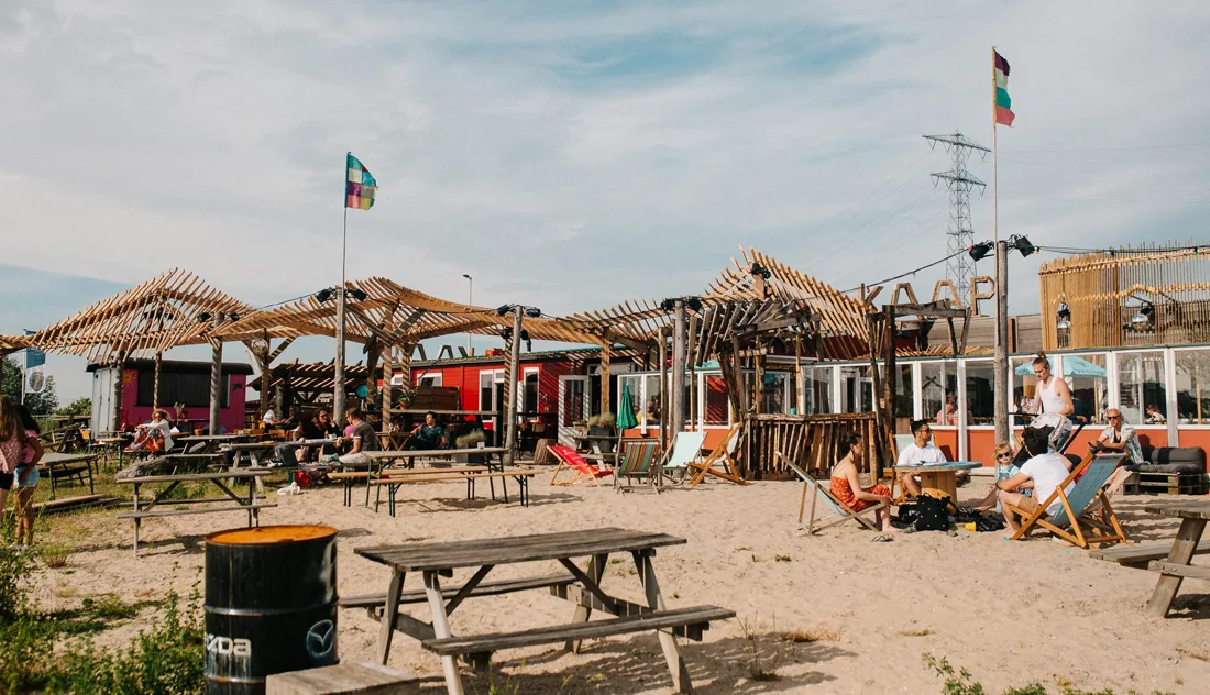 Kaap Amsterdam sandy beach terrace with timber pergolas, picnic benches and KAAP sign