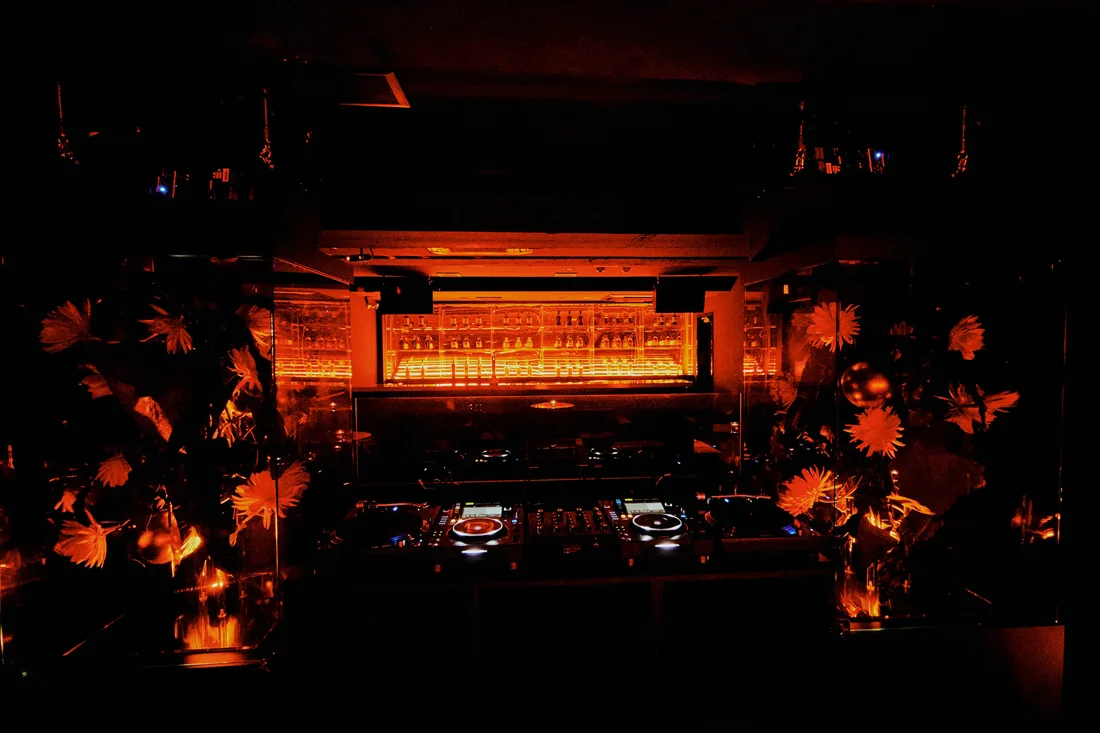 Mitsuki dark floor with DJ booth, orange-lit bar and flowers
