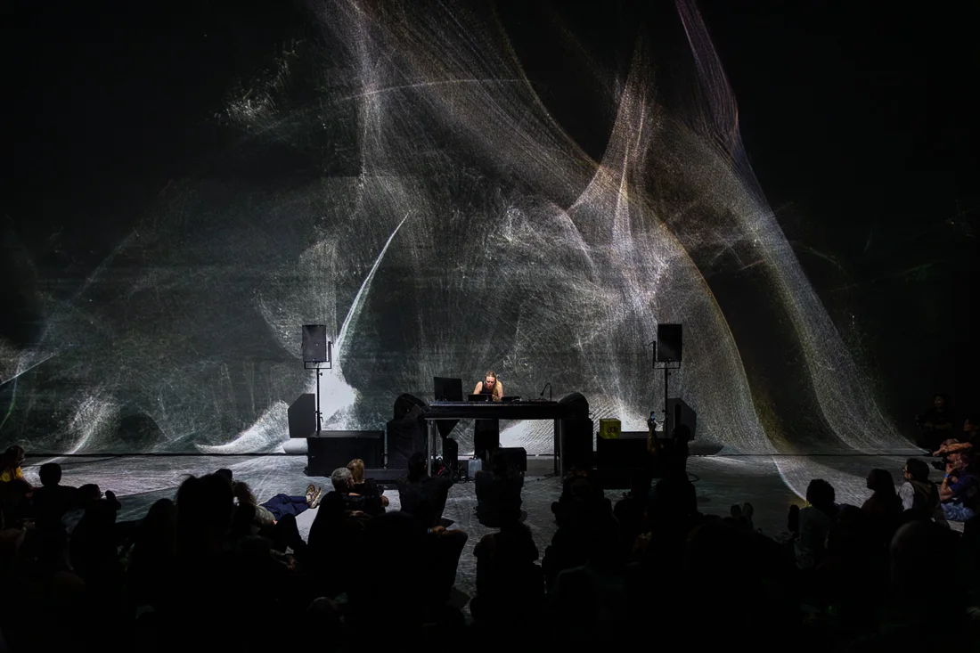 Nxt Museum hall with DJ before a giant projection, seated audience