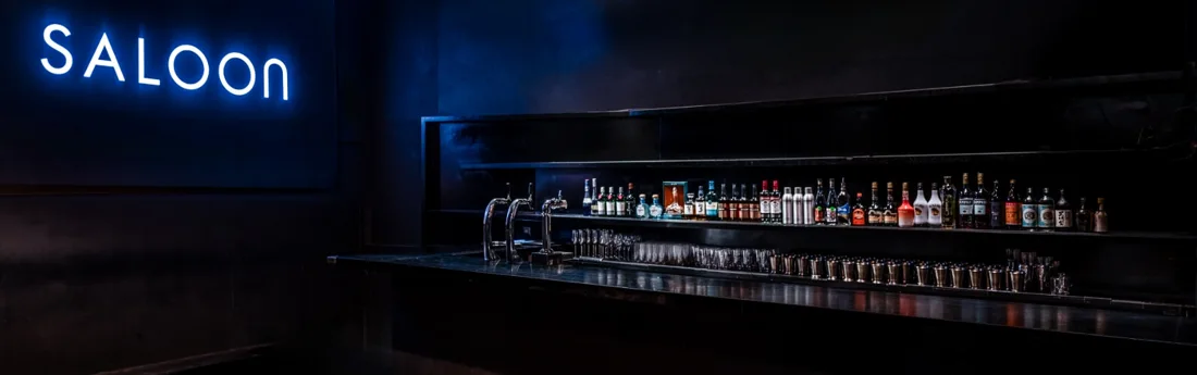 Saloon back bar with neon SALOON sign and bottle shelves