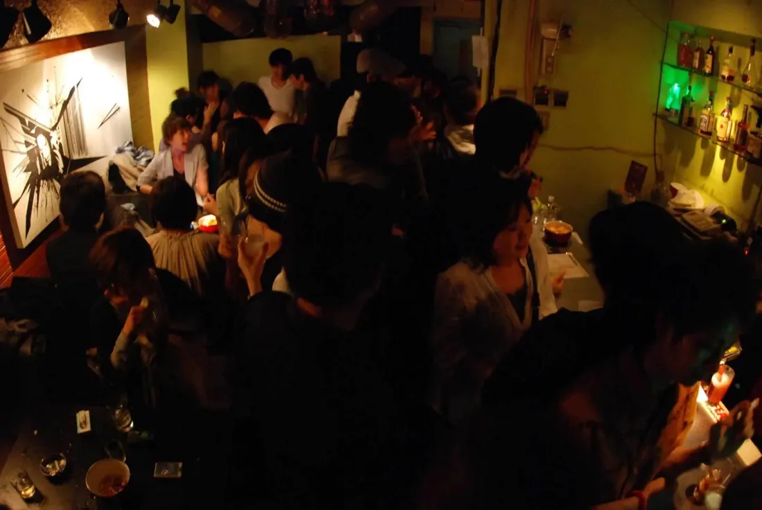 Shibuya OTO bar room crowded, mural wall and lit bottle shelf