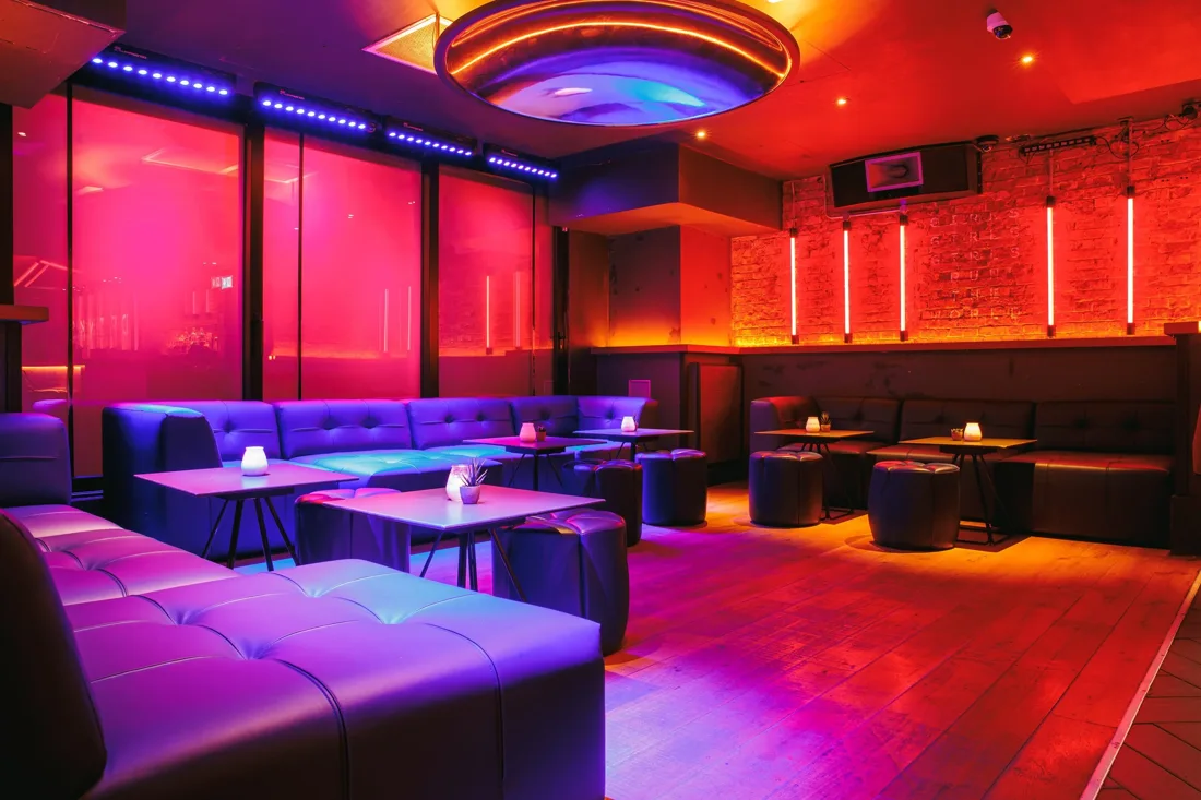 The Roxy lounge with purple banquettes, tables and lit brick wall