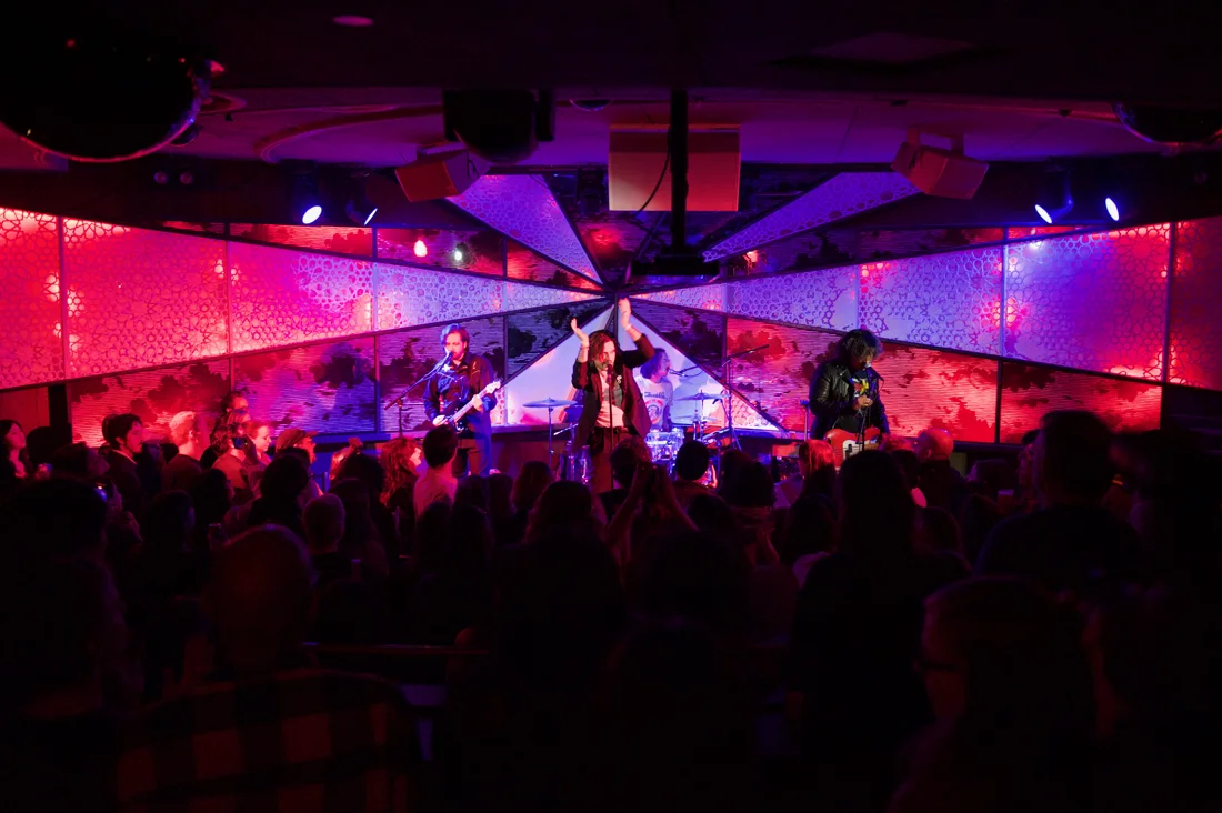 The Sultan Room stage and kaleidoscope mirror wall lit pink, crowd in front