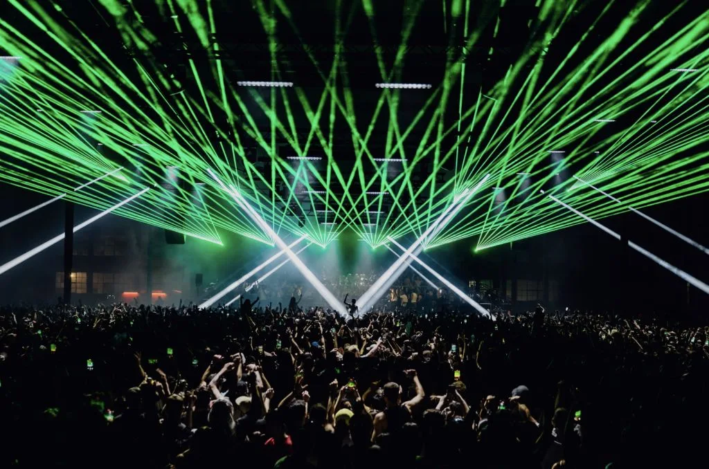 A crowd beneath green laser lighting inside The Wool Store